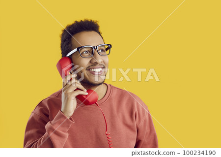 Happy young African American man talking to friends on landline phone and smiling Happy young African American man talking to friends on landline phone and smiling 100234190
