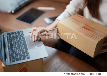 Starting small business entrepreneur of independent young Asian woman online seller is using computer and taking orders to pack products for delivery to customers. SME delivery concept. Starting small business entrepreneur of independent young Asian woman online seller is using computer and taking orders to pack products for delivery to customers. SME delivery concept. 100234818