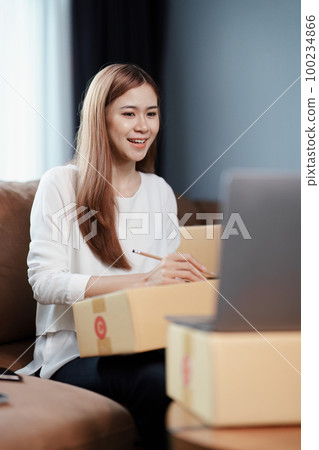 Starting small business entrepreneur of independent young Asian woman online seller is using computer and taking orders to pack products for delivery to customers. SME delivery concept. Starting small business entrepreneur of independent young Asian woman online seller is using computer and taking orders to pack products for delivery to customers. SME delivery concept. 100234866