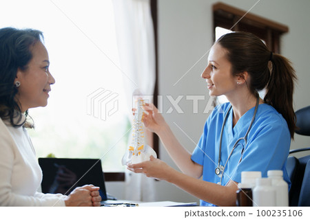 Portrait of a female doctor talking to an elderly patient about herniated disc deterioration from long hours of work 100235106