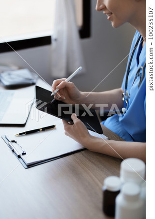 Portrait of a female doctor using a tablet computer and a document analyzing a patient's condition before treating 100235107