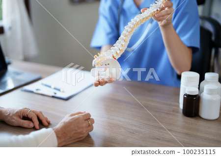 Portrait of a female doctor talking to an elderly patient about herniated disc deterioration from long hours of work 100235115