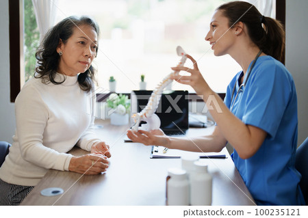 Portrait of a female doctor talking to an elderly patient about herniated disc deterioration from long hours of work 100235121