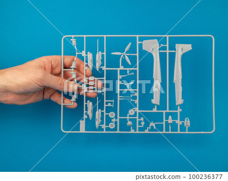 Sprue from a plastic model kit in hand on the blue background. Parts tree of the airplane model. Building model aircraft, hobby concept 100236377
