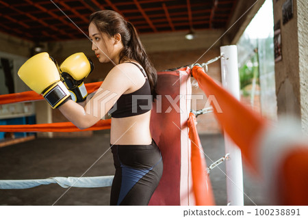 a female boxer standing with punching moves inside the box ring a female boxer standing with punching moves inside the box ring 100238891