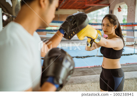 a female boxer punching the pad weared by the coach 100238941