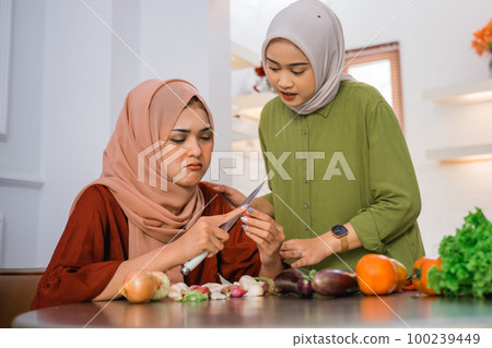 sad woman in hijab peeling onions and her friend sympathizing sad woman in hijab peeling onions and her friend sympathizing 100239449