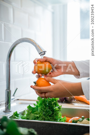 Woman's hand washing tomatoes with running water in the sink 100239454