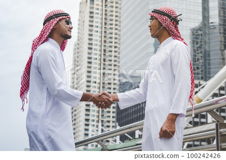 Arab Businessman Muslim dress shaking hands together. Muslim Men Teamwork business partner handshake with business Partnership. Close up hand UAE diversity multiracial people trust honesty commitment 100242426