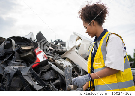 Mechanical woman owner small business inspecting standing in the car junkyard, Dirty male repairman choosing spare parts on car junkyard, Used of vehicle part for recycling in the scrap yard garage. 100244162