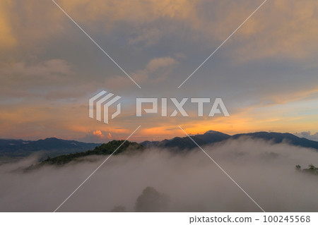 aerial view beautiful yellow sunrise above the mountain in phang Nga valley. slow floating fog blowing cover on the mountain look like as a sea of mist. scenery golden sunrise at horizon background. aerial view beautiful yellow sunrise above the mountain in phang Nga valley. slow floating fog blowing cover on the mountain look like as a sea of mist. scenery golden sunrise at horizon background. 100245568
