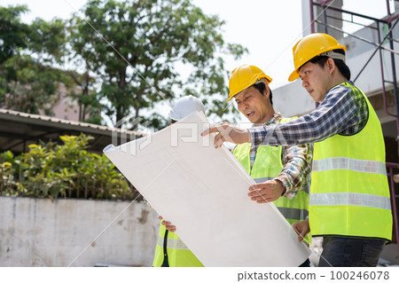 Asian engineer or Young Female Architect put on a helmet for safety and talk with a contractor on a construction building factory project, Concept of Teamwork, Leadership concept. 100246078