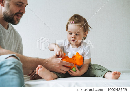 Happy father and baby girl little daughter having fun playing with toy in children room at home Happy father and baby girl little daughter having fun playing with toy in children room at home 100248759