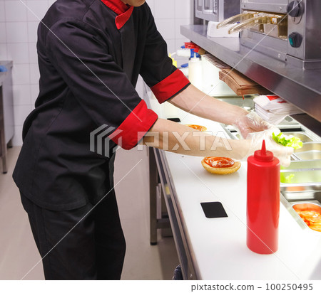 Cook adding a ketchup on burger. Cook adding a ketchup on burger. 100250495