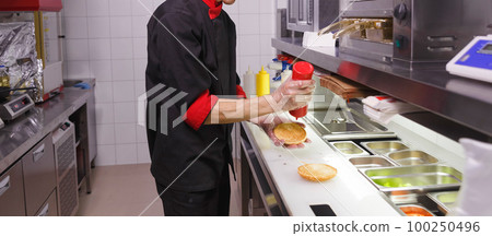 Cook adding a ketchup on burger. 100250496