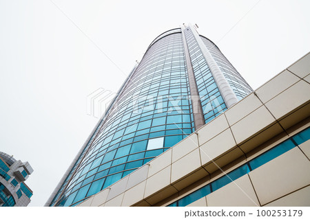 Skyscraper facade with blue glass windows on white rain clouds background. View from below, perspective. Skyscraper facade with blue glass windows on white rain clouds background. View from below, perspective. 100253179