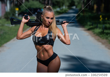 Caucasian woman in bikini with machine gun outdoors. 100254509
