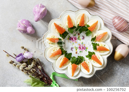 Festive dinner, Easter brunch. Stuffed eggs with cheese and salted salmon in the form of a carrot. View from above. Festive dinner, Easter brunch. Stuffed eggs with cheese and salted salmon in the form of a carrot. View from above. 100256702