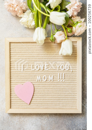 Happy Mother's Day. Letter I LOVE MOM with heart on letterboard and beautiful spring flowers. Womans day, wedding, mothers day greeting card. View from above. 100256739
