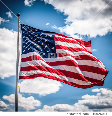 the American flag develops against the background of a blue sky with clouds 100260619