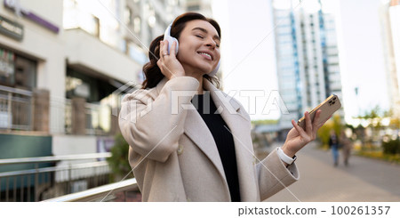 happy peaceful girl tourist enjoys music in wireless headphones while walking on the street 100261357