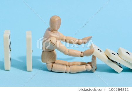 A wooden puppet toy holds back a falling domino on a blue background, representing the concept of a strong personality A wooden puppet toy holds back a falling domino on a blue background, representing the concept of a strong personality 100264211