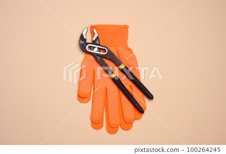 Orange glove and metal universal adjustable wrench on a beige background, top view Orange glove and metal universal adjustable wrench on a beige background, top view 100264245