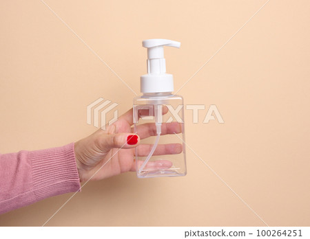 Female hand holds empty plastic container with dispenser for liquid products, soap or shampoo on beige background Female hand holds empty plastic container with dispenser for liquid products, soap or shampoo on beige background 100264251