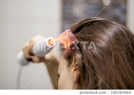 Woman uses darsonval for massage head's skin. 100264864