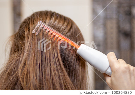 Woman uses darsonval for massage head's skin. 100264880