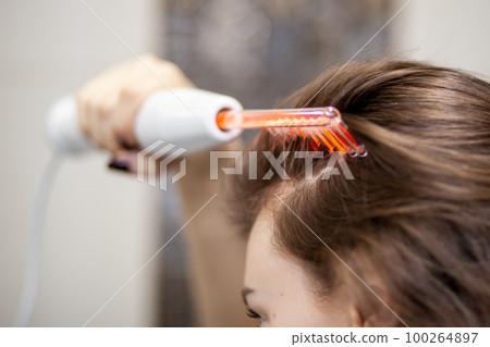 Woman uses darsonval for massage head's skin. 100264897