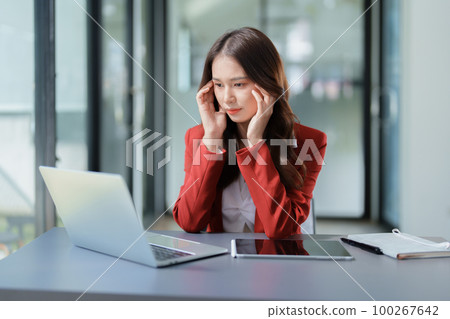 A portrait of a beautiful Asian female employee showing a stressed face while using the phone and financial documents on her desk. A portrait of a beautiful Asian female employee showing a stressed face while using the phone and financial documents on her desk. 100267642
