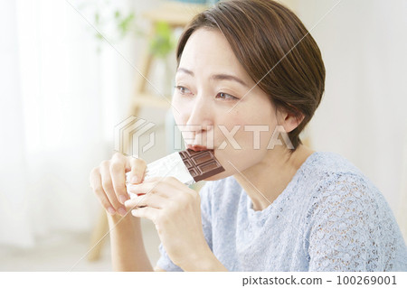 Woman eating chocolate at home 100269001