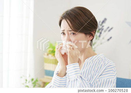 Woman blowing her nose in the living room Woman blowing her nose in the living room 100270528