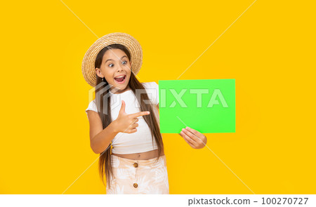 happy teen girl with copy space on green paper on yellow background. pointing finger 100270727