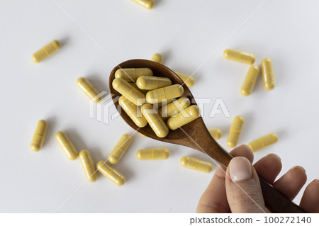 Transparent capsules with yellow-beige powder inside. A supplement or tablet for liver health. A full spoonful of medicine with a white background and scattered medications. 100272140