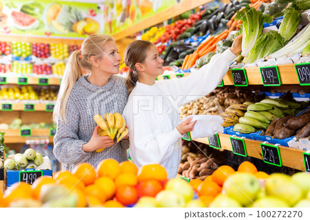 Smiling teenage girl with mother choosing fruits and vegetables in supermarket Smiling teenage girl with mother choosing fruits and vegetables in supermarket 100272270