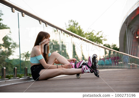 Skater girl puts on roller skates on the bridge. 100273196