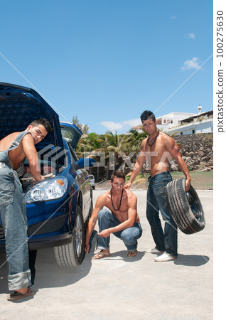 young attractive men changing the wheel of theirs car in the sunshine 100275630