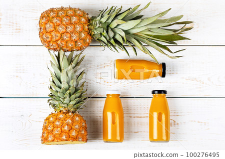 Two pineapples and a fresh healthy smoothie in a glass bottle on a white wooden background. Healthy, detox and dietary nutrition concept. Two pineapples and a fresh healthy smoothie in a glass bottle on a white wooden background. Healthy, detox and dietary nutrition concept. 100276495