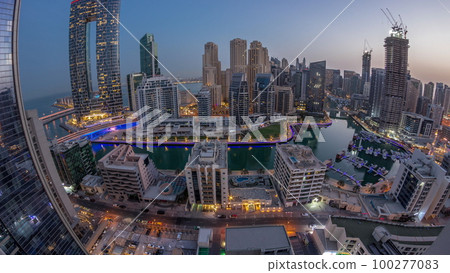 Panorama of Dubai Marina with several boats and yachts parked in harbor and skyscrapers around canal aerial night to day timelapse. 100277083