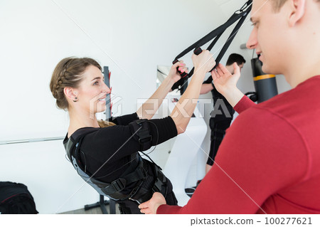 Trainer working with woman in ems gym on sling equipment 100277621