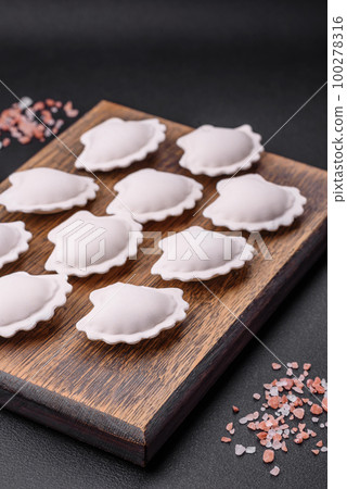 Raw frozen stuffed dumplings on a wooden cutting board 100278316