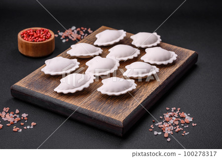 Raw frozen stuffed dumplings on a wooden cutting board Raw frozen stuffed dumplings on a wooden cutting board 100278317