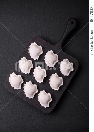 Raw frozen stuffed dumplings on a wooden cutting board Raw frozen stuffed dumplings on a wooden cutting board 100278323