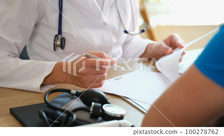 Doctor makes notes in document, sitting at table with patient. 100278762