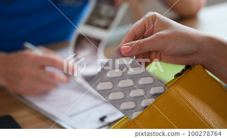Doctor checks results of ultrasound at table with patient, who holds pills in her hand. 100278764
