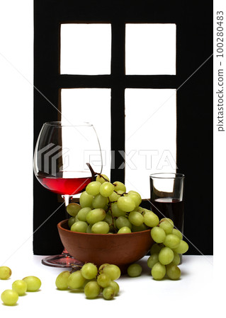 A bunch of ripe grapes in a plate with a drink in a glass by the window A bunch of ripe grapes in a plate with a drink in a glass by the window 100280483