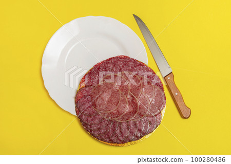 Smoked sausage of different varieties and a knife on a yellow background 100280486