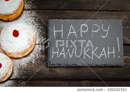 Happy Hanukkah. Traditional dessert Sufganiyot on dark wooden background. Donuts, candles and gifts. Celebrating Jewish holiday. 100282562